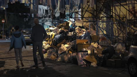 Night-walk-past-piled-waste-in-Naples,-Italy
