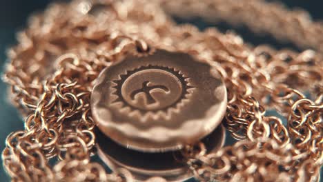 A-detailed-crispy-macro-shot-of-a-golden-medallion-necklace,-flying-bird-in-the-middle-of-the-sun-symbol,-on-a-rotating-stand,-mirror-reflection,-studio-lighting,-4K-video