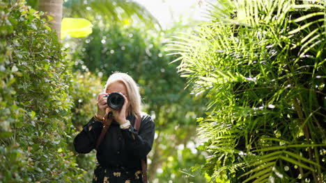 Blonde-Photographer-Taking-Photos-In-Tropical-Garden-Setting-With-DSLR-Camera,-4K-Resolution,-Slow-Motion