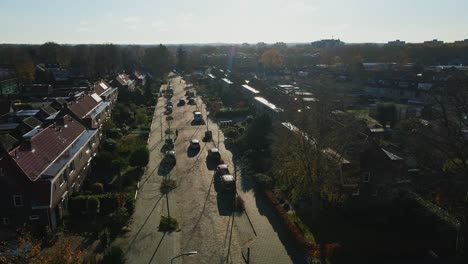 Low-aerial-of-cars-driving-over-a-calm-street-in-a-peaceful-suburban-neighborhood-on-a-sunny-autumn-day