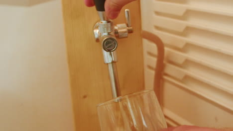 Pouring-beer-with-bubbles-and-foam-in-glass-from-tap-with-hand-holding-it