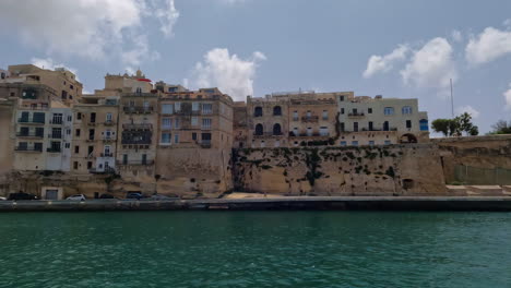 -Valetta,-Ciudad-De-Malta,-Edificios-De-Apartamentos-Costeros-Desde-Un-Barco-En-Movimiento
