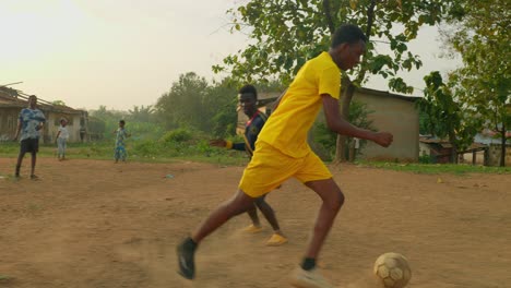 Young-man-with-a-yellow-jersey-successfully-dribbles-through-a-defender-but-fails-to-make-a-goal-as-the-goalkeeper-stops-his-attempt,-community-soccer-field,-Kumasi,-Ghana