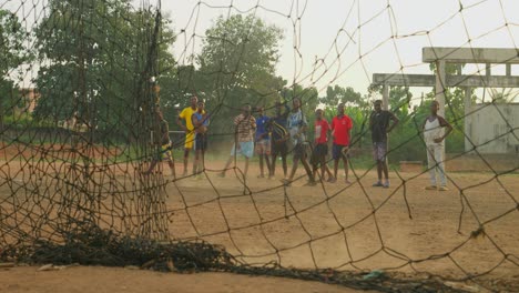 Young-man-as-a-goal-keeper-stops-the-ball-and-tosses-it-to-the-left-as-others-take-turns-practicing-free-kicks,-community-soccer-field,-Kumasi,-Ghana