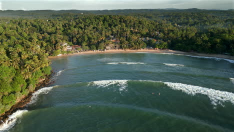 Establecimiento-De-Toma-Aérea-De-Drones-De-La-Playa-Y-Bahía-De-Hiriketiya-Con-Surfistas-En-El-Agua-Y-Olas-Rompiendo-En-La-Costa-Sur-Tropical-De-Sri-Lanka