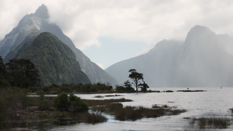 Panorama-of-Milford-Sound,-majestic-cloud-shrouded-peaks-rise-from-the-depths-of-a-mirror-like-fiord