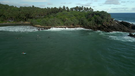 Establecimiento-De-Una-Toma-Aérea-Con-Drones-De-La-Bahía-De-Hiriketiya-Con-Surfistas-Balanceándose-Y-Flotando-En-El-Sur-De-Sri-Lanka