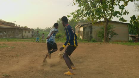 Junger-Mann-Dribbelt-Den-Ball-Durch-Trikot-Nummer-Sechs-Und-Eins-Mit-Blauem-Hemd-Und-Schießt-Den-Ball-Dann-In-Richtung-Tor,-Gemeinschaftsfußballfeld,-Kumasi,-Ghana