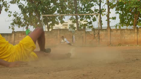 Abgenutzter-Fußball,-Der-Für-Einen-Freistoß-Bereit-Ist,-Dann-Schießt-Ein-Junger-Mann-Mit-Einem-Gelben-Trikot-Ihn-In-Richtung-Tor-Und-Der-Torwart-Schafft-Es-Nicht,-Ihn-Zu-Fangen,-Gemeinschaftsfußballplatz,-Kumasi,-Ghana