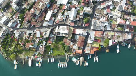 Drone-top-down-descends-on-coastal-village-by-Lake-Atitlan-Guatemala-with-boats-docked-at-pier