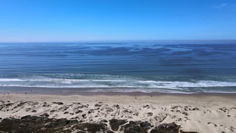 Experience-the-tranquil-beauty-of-the-coast-with-this-stunning-view-of-blue-ocean-waves,-clear-skies,-and-sandy-beach-dunes-in-the-foreground