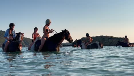 People-on-vacation-enjoy-riding-horses-in-sea-water-in-summer-season-in-Corsica,-France