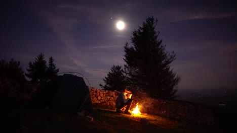Man-eats-alone-at-tent-camp-bonfire-with-full-moon-light-in-wilderness