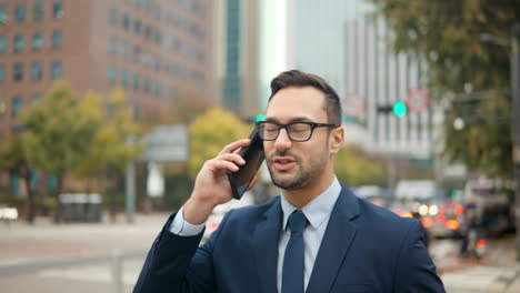 Businessman-walking-down-city-sidewalk,-talking-on-phone