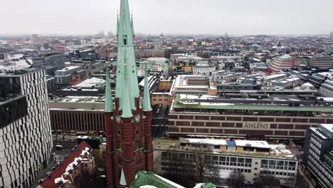 Drone-ascends-tilting-down-along-historic-gothic-styled-brown-and-white-brick-church-in-Stockholm-city-center