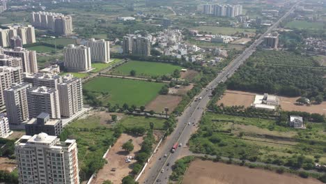 RAJKOT-CITY-AERIAL-VIEW-KALAWAD-ROAD-DRONE-TOP-ANGLE-SHOWING-LOTS-OF-LOW-RISE-BUILDINGS-AND-HIGH-RISE-BUILDINGS-BETWEEN-TREES,-LARGE-FARMS-AROUND-THE-BUILDINGS