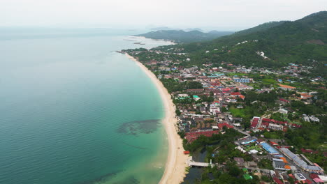 Aerial-view-of-Maret-village-with-sandy-beach,-clear-water-of-ocean-and-green-mountains-on-Koh-Samui-Island,-Surat-Thani,-Thailand