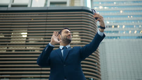 Businessman-in-big-city-holding-phone,-waves-goodbye-to-someone-on-video-call