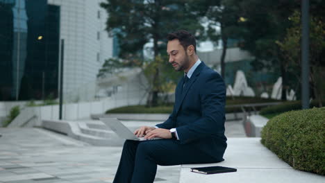 Businessman-sitting-in-courtyard,-typing-on-laptop-computer