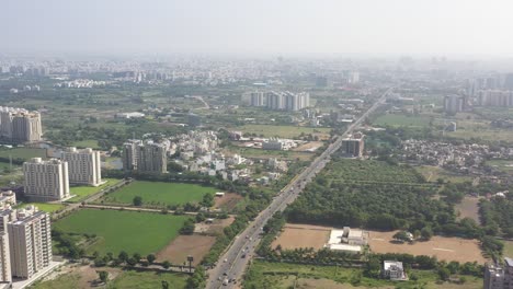 RAJKOT-CITY-AERIAL-VIEW-A-drone-is-flying-over-the-Kalavad-road,-where-many-complexes-and-box-crickets-are-visible-on-the-road-surrounded-by-dense-trees