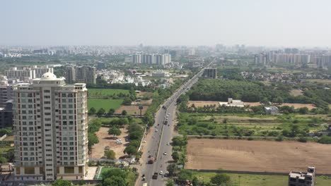 RAJKOT-CITY-AERIAL-VIEW-Drone-flying-in-the-middle-of-Kalawad-Road-from-the-side-of-the-camera,-with-residential-houses-and-bungalows-on-its-right-side