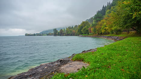 Lake-Attersee-Austria-coastal-waters-with-cloudy-sky-above-autumn-forest