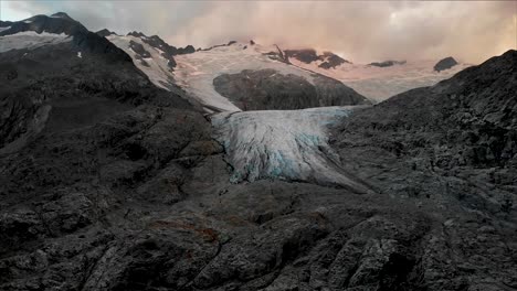 Aerial-flight-over-the-glacial-lake-starting-with-an-up-close-view-of-the-of-the-Gauli-glacier-in-the-Bernese-Oberland-region-of-the-Swiss-Alps-as-the-sun-sets-on-a-cloudy-day