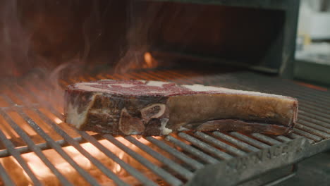 Chef-hand-drops-big-slice-of-dry-Australian-beef-steak-onto-metal-grill-with-fire-and-flames