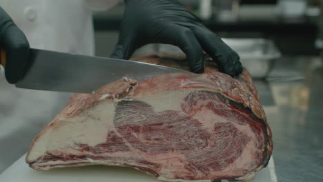 Close-up-on-chef-hand-slicing-huge-Australian-dry-beef-meat-with-kitchen-knife