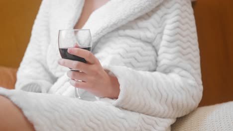 A-woman-relaxing-holding-a-red-wine-glass-wearing-robe