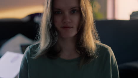 Cinematic-Close-up-of-a-young-white-Woman-smiling-and-waving-straight-into-the-Camera-during-a-golden-hour-Sunrise-in-her-apartment-in-the-morning-in-slow-motion
