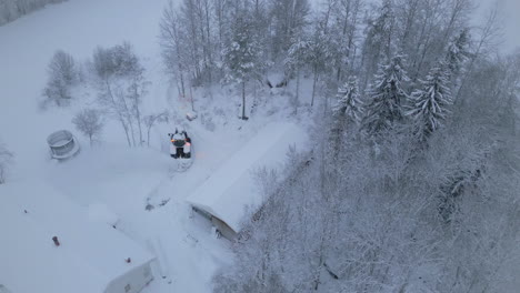 Tractor-Arando-Nieve-Para-Casa-Forestal-En-El-Paisaje-Invernal-ártico,-Vista-Aérea