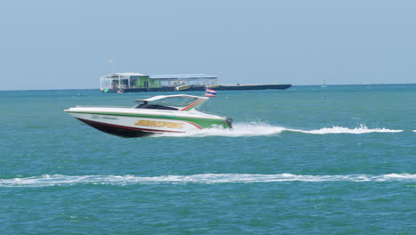 Ein-Schnell-Fahrendes-Boot-Mit-Einer-Thailändischen-Nationalflagge,-Das-Nach-Links-Fährt-Und-Wildwasser-Und-Andere-Boote-Im-Hintergrund-Freigibt,-Pattaya,-Thailand