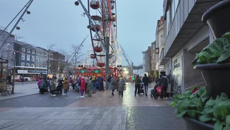 Street-in-Cork-city,-evening-in-winter-people-gathered-around-lit-Ferris-wheel-in-Ireland