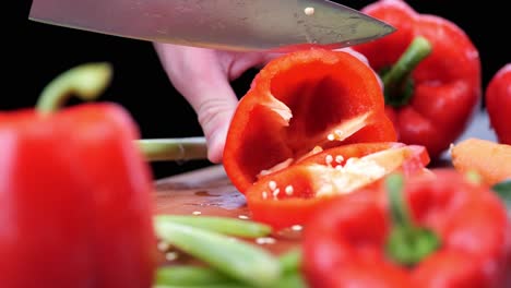 Chef-with-sharp-knife-cuts-fresh-peppers-on-wooden-chopping-board-surrounded-by-various-vegetables