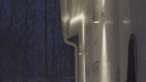 Snowfall-at-night-near-glowing-building-exterior,-static-view