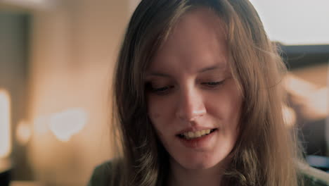 Cinematic-close-up-of-a-Young-White-Woman-smiling-straight-into-the-camera-during-a-golden-hour-Sunrise-in-her-apartment-in-slow-motion