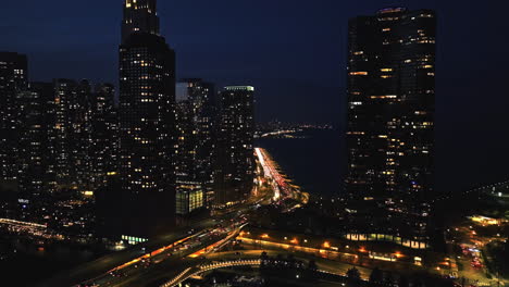 Aerial-tracking-shot-of-traffic-in-middle-of-skyscrapers-on-the-illuminated-lakefront-of-Chicago