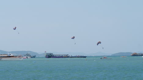 Three-people-parasailing-in-Pattaya-as-they-are-being-pulled-by-boat-to-gain-altitude-while-are-other-boats-are-seen,-Thailand