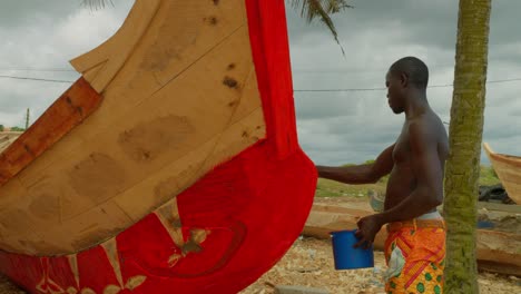 Hombre-Negro-Africano-Pintando-Un-Barco-De-Madera-Para-Pescar-En-Una-Remota-Aldea-De-Ghana
