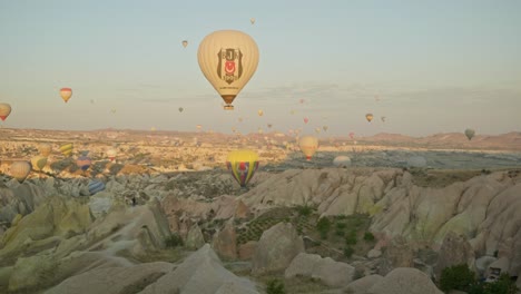 Hot-air-balloons-fly-over-rocky-sun-kissed-morning-landscape
