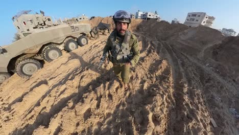 Israeli-soldier-running-through-Gaza-desert-with-rifle-passing-armoured-vehicles
