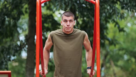 Young-athletic-sportsman-doing-pull-ups-at-red-sports-facility-in-park