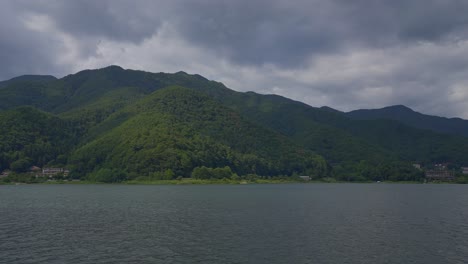 Traverse-the-serene-lake,-where-the-vista-unfolds-with-green-hills-cascading-into-the-Japanese-waters-from-the-boat's-viewpoint-during-a-cloudy-day