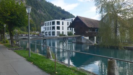 Interlaken-Immersive-POV:-Moving-Through-Early-Morning-City-Streets-In-Switzerland,-Europe,-Walking-|-Shaky-Movement-From-Small-Path-to-Small-Mill-on-Turquoise-Water-Front