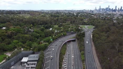 Aerial-view-of-a-major-highway-with-roundabout-and-a-tunnel-entrance-city-skyline-in-the-background