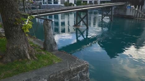 Interlaken-Immersive-POV:-Moving-Through-Early-Morning-City-Streets-In-Switzerland,-Europe,-Walking-|-Shaky-Dramatic-Reveal-From-Small-Bridge-to-Turquoise-Water