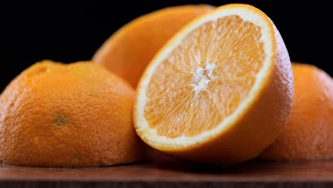 Freshly-cut-oranges-in-front-of-black-background-on-cutting-board,-close-up-pan