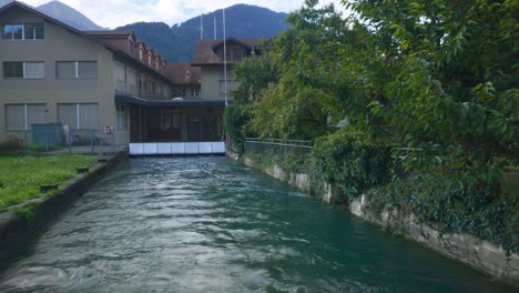 Interlaken-Immersive-POV:-Bewegung-Durch-Die-Straßen-Der-Stadt-Am-Frühen-Morgen-In-Der-Schweiz,-In-Europa,-Zu-Fuß-|-Zitternde-Bewegung-Vom-Kleinen-Weg-Zur-Brücke-Am-Wasser