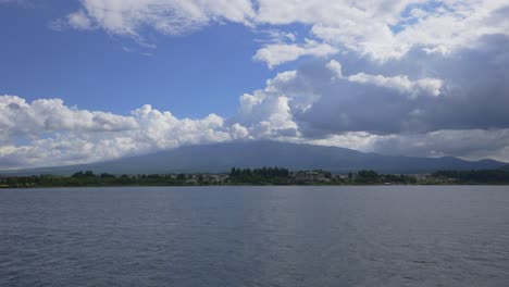 Traverse-the-tranquil-waters-on-a-boat,-witnessing-Fuji-mountain-enveloped-in-clouds-during-daylight